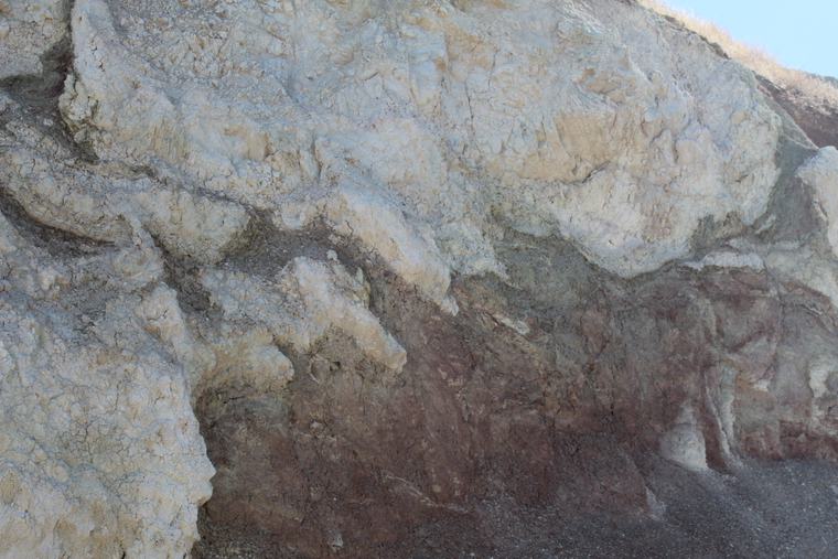 A pale altered unit exposed in a cliff face, sharply bounded against darker rock