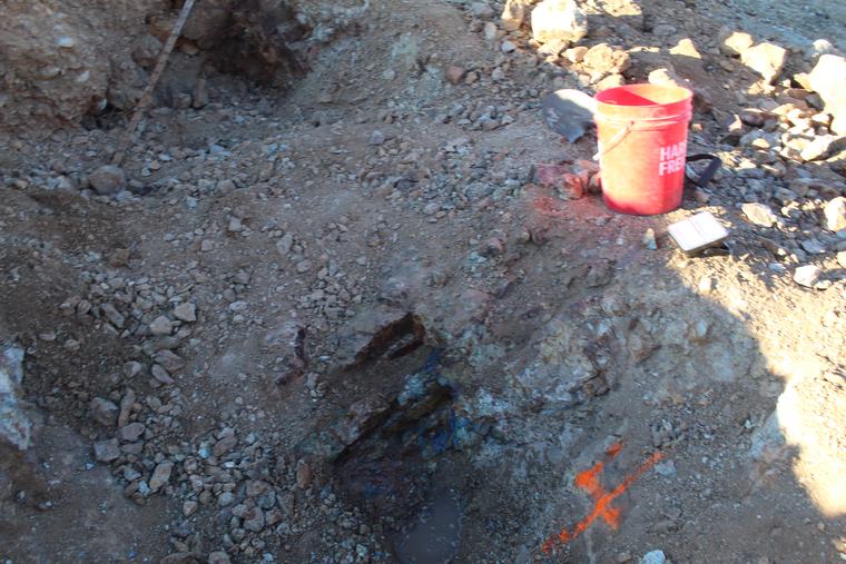 Tools beside a shallow pit exposing copper-stained rock