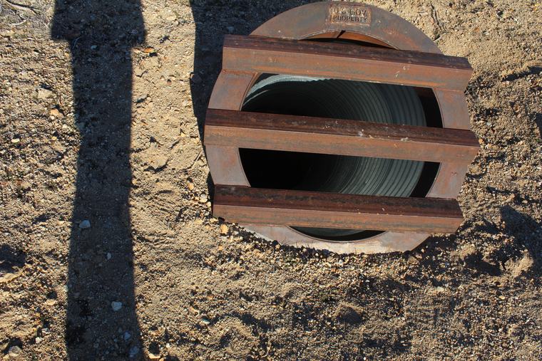 A steel grate stamped U.S. GOV PROPERTY capping a culvert shaft closure